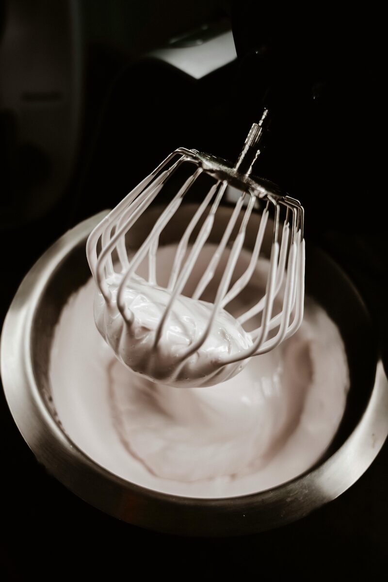 Whisk lifted from a bowl of glossy whipped peaks