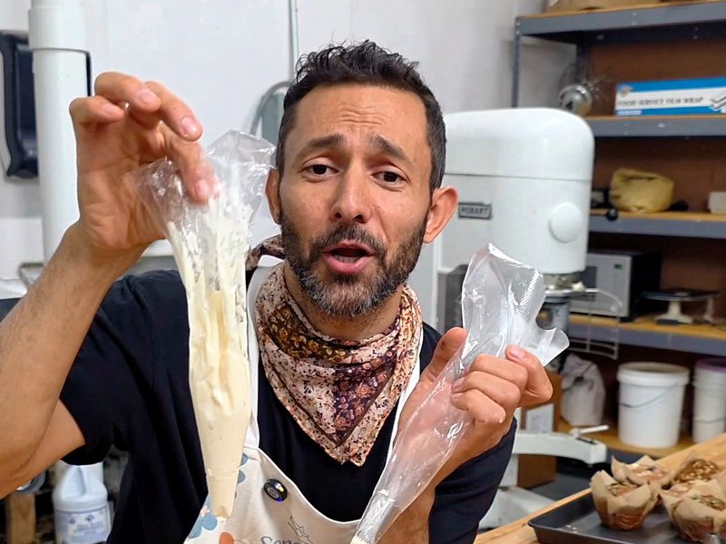Wassem snipping the tip off a piping bag with scissors in the bakery