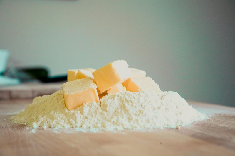 Cubes of cold butter sitting on a mound of flour on a wooden board