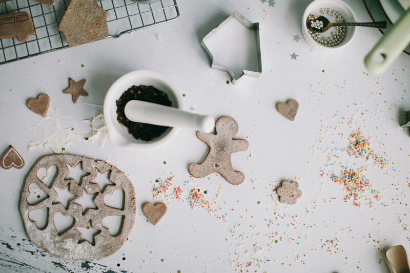 Rolled cookie dough with cutters, sprinkles, and a mortar of spices on a white surface