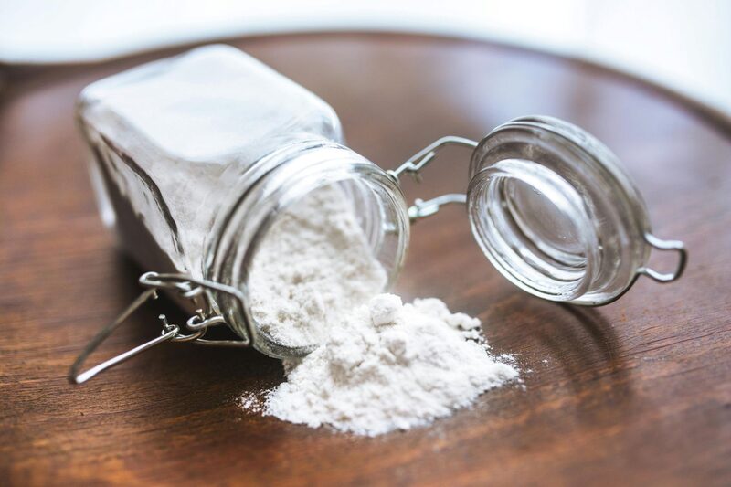 Open jar of baking soda spilled on a wooden surface