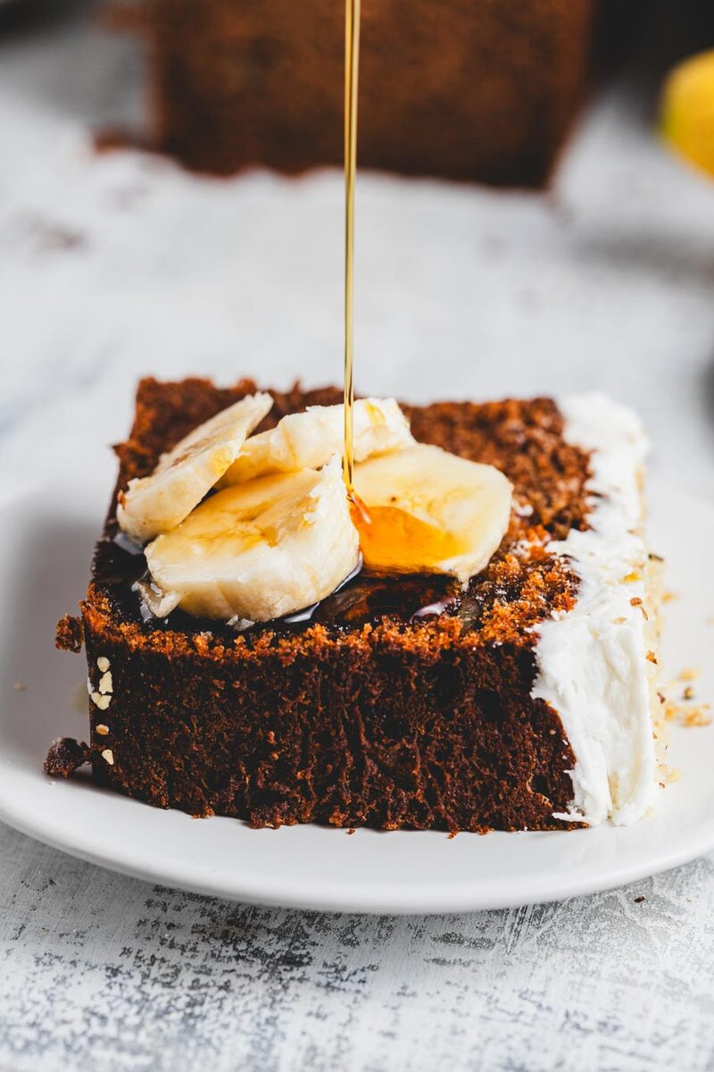 A slice of banana loaf cake topped with fresh banana and a drizzle of syrup