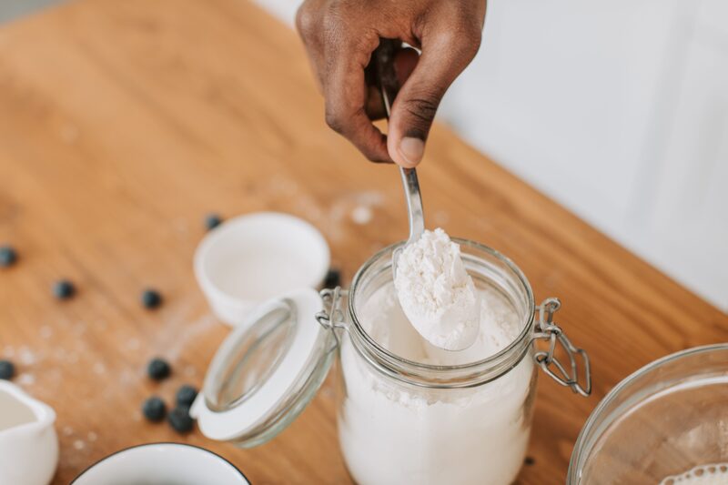 A spoon lifting white leavening powder from a glass jar