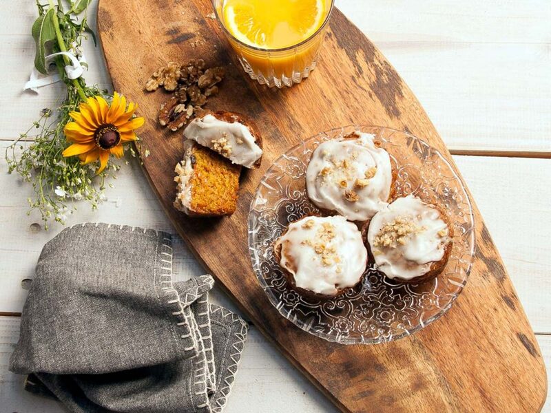 Iced carrot walnut muffins on a wooden board with orange juice and walnuts