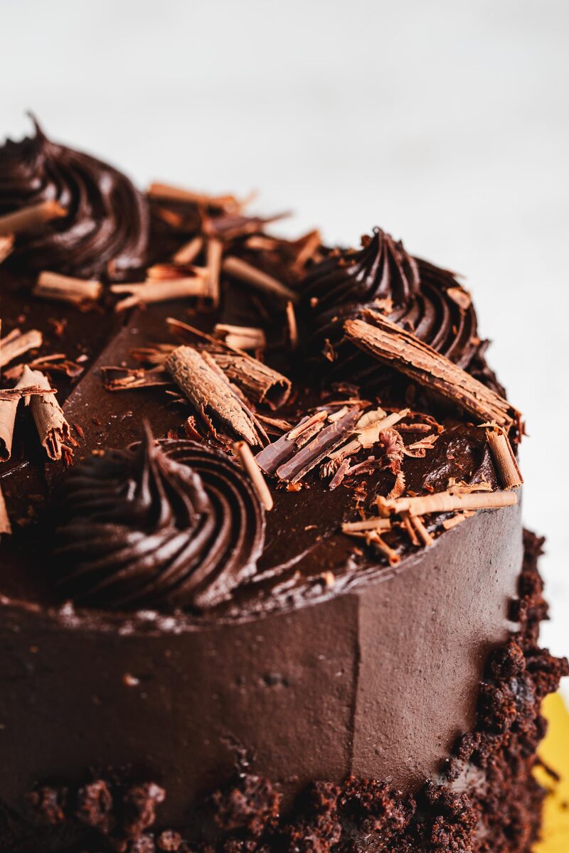 Close-up of a layer cake finished in dark chocolate frosting with piped swirls and chocolate curls