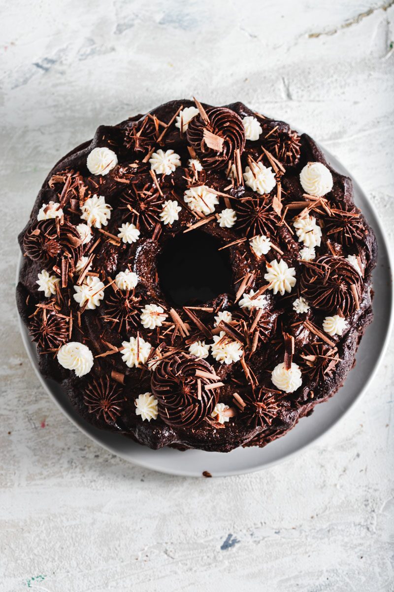 Top-down view of a bundt cake covered in dark chocolate frosting, piped rosettes and chocolate shavings