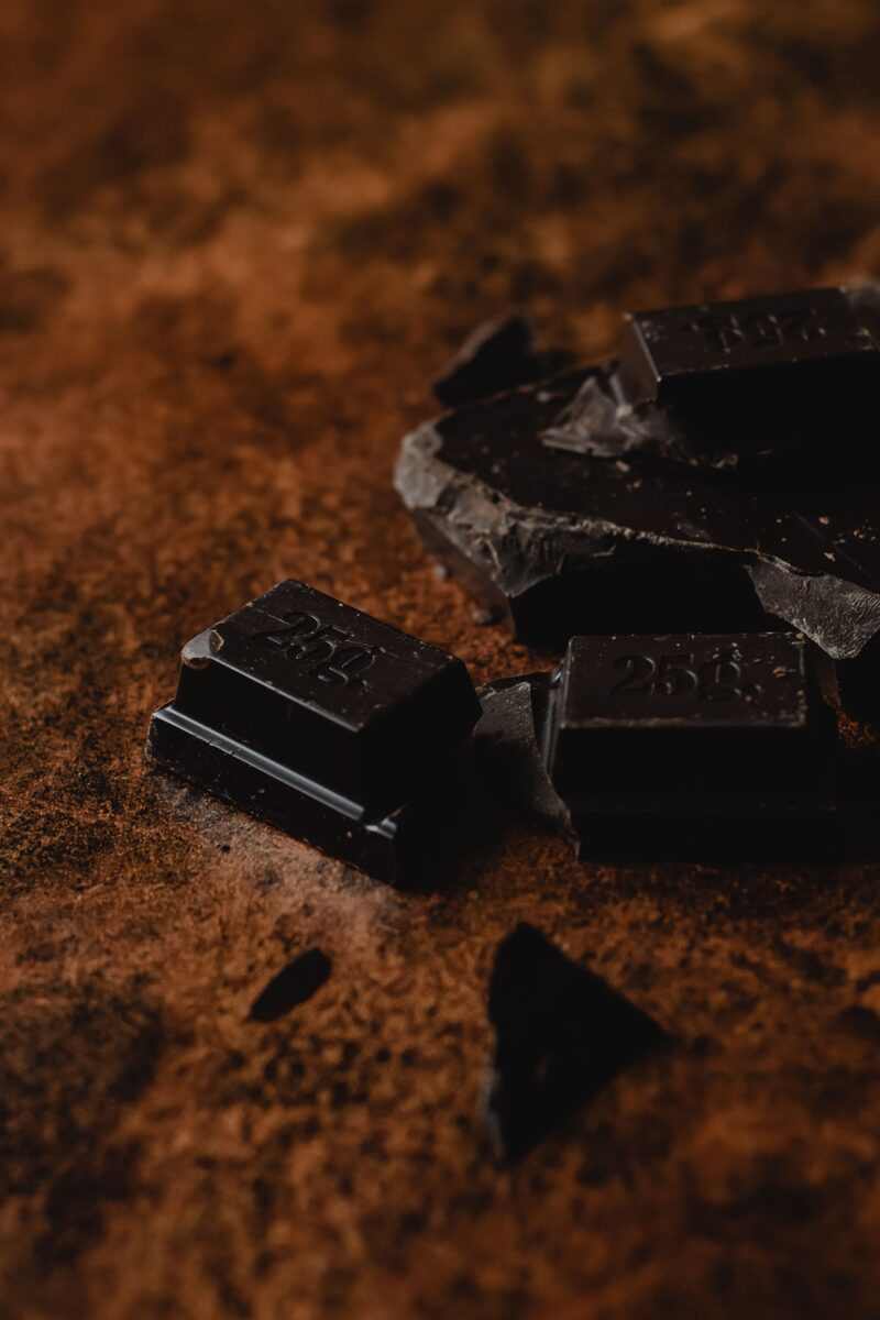 A bowl of cocoa powder surrounded by cacao beans and chocolate