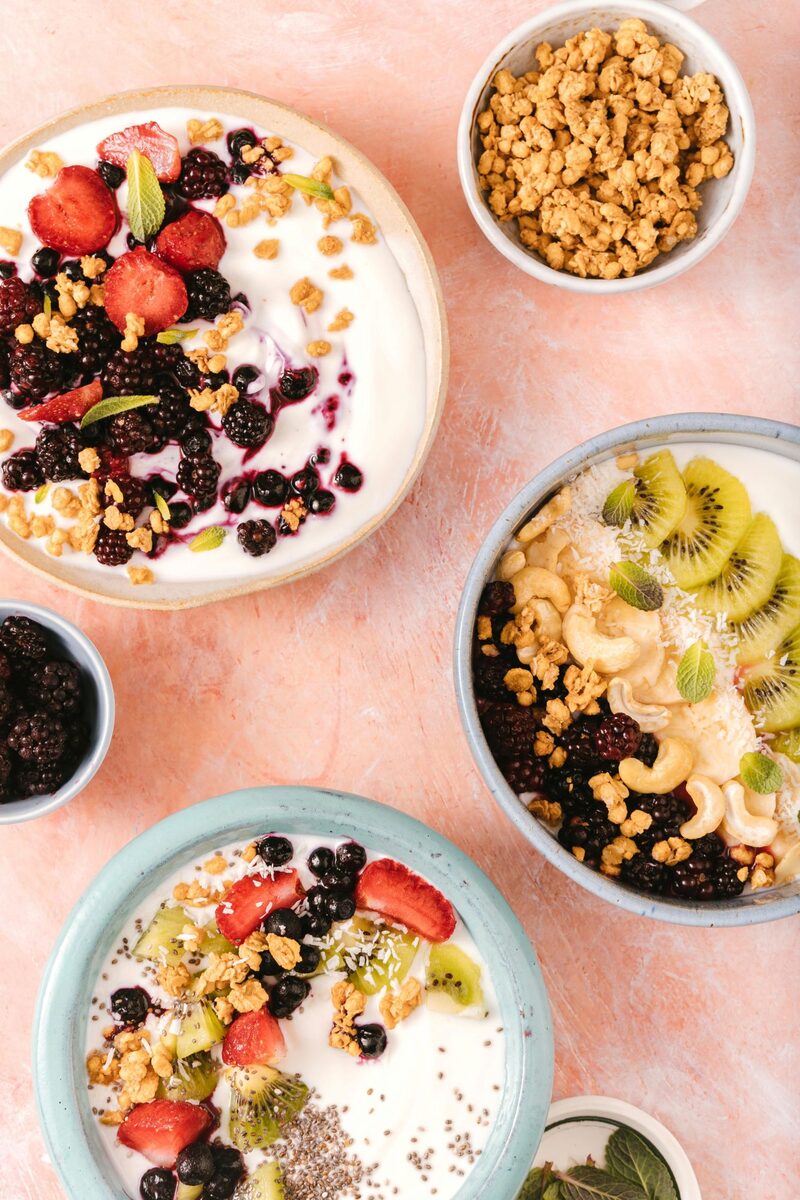 Bowls of yogurt topped with berries, kiwi, and granola