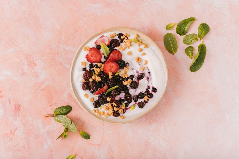 A bowl of coconut yogurt topped with berries, granola, and mint