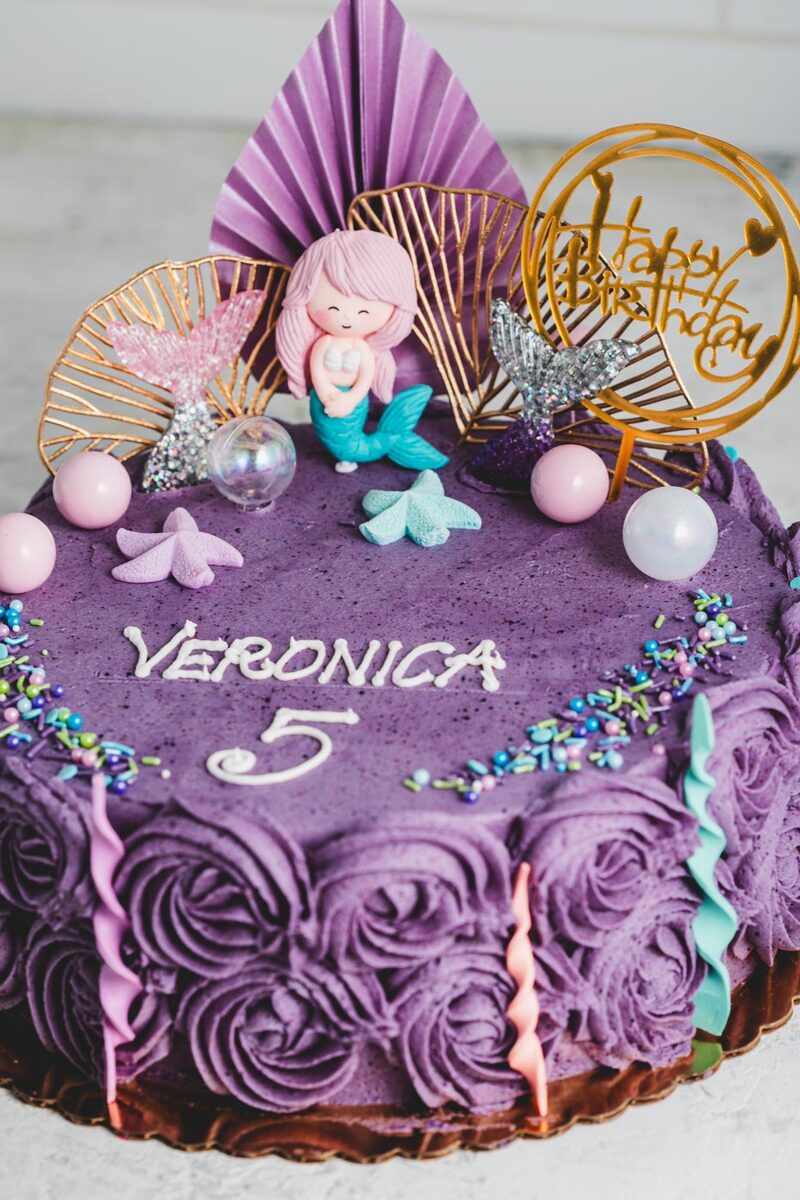 Whimsical purple buttercream birthday cake decorated with a mermaid topper and pastel sprinkles