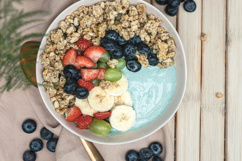 Bright blue spirulina smoothie bowl topped with granola, banana, and berries