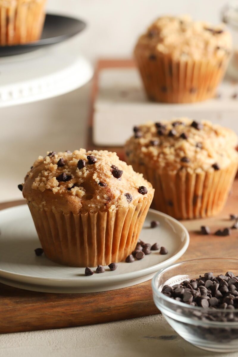 Chocolate chip muffins on a plate with mini chocolate chips scattered on a wooden board