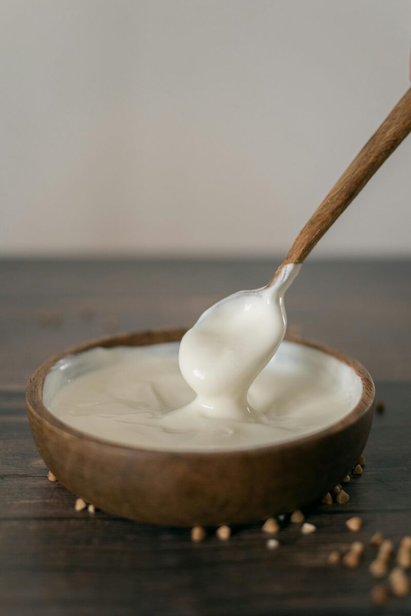 Wooden bowl of thick, creamy DIY yogurt substitute being scooped with a wooden spoon