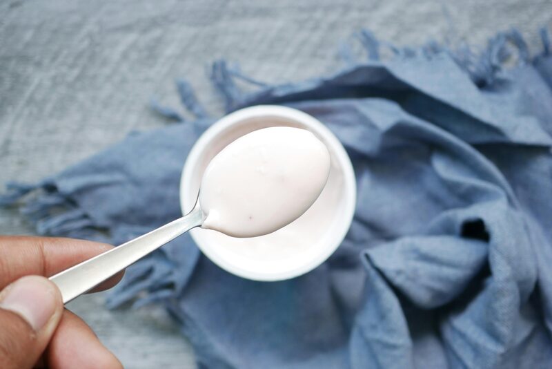 Spoonful of DIY yogurt substitute held over a small white ramekin on a blue linen cloth