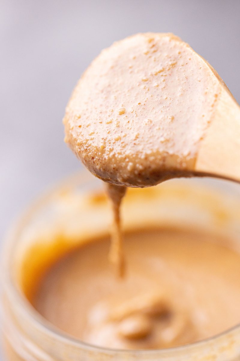 A spoon lifting a thick scoop of peanut butter that holds its shape with a slow drip back into the jar