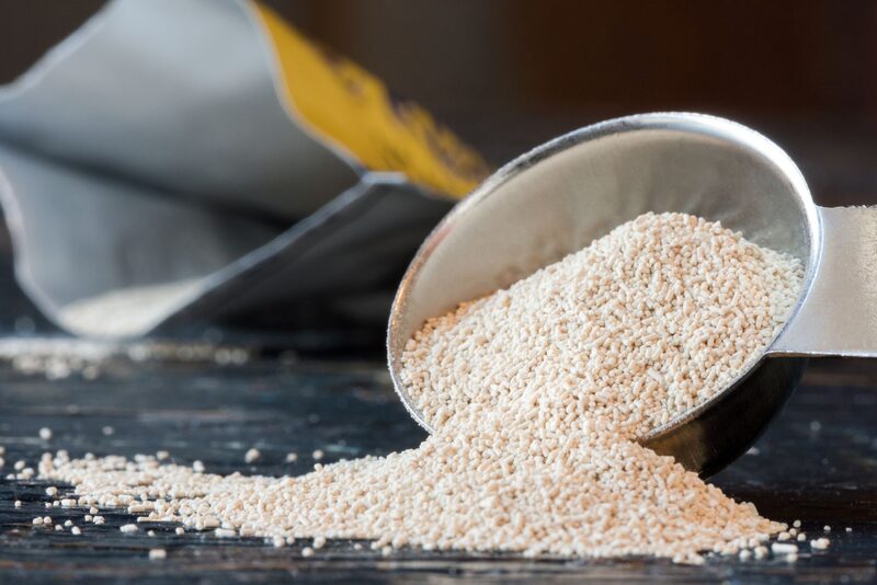 A metal scoop spilling dried yeast granules onto a wooden surface