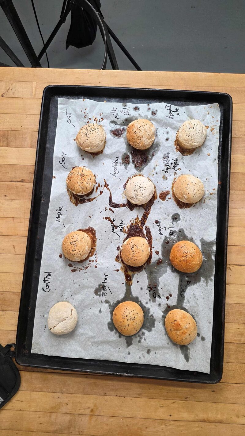 A tray of vegan gluten free bread rolls testing different egg wash alternatives, each labeled in marker on the parchment