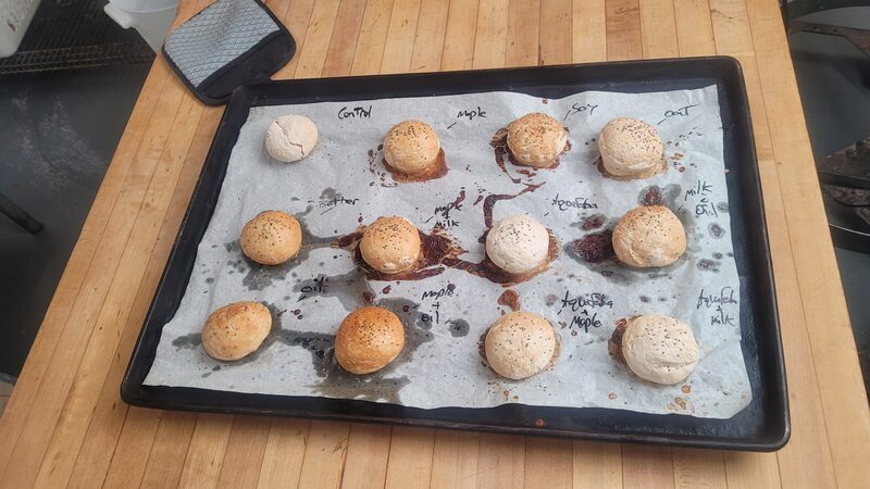 A baked tray of gluten-free vegan rolls labeled with each egg wash alternative tested