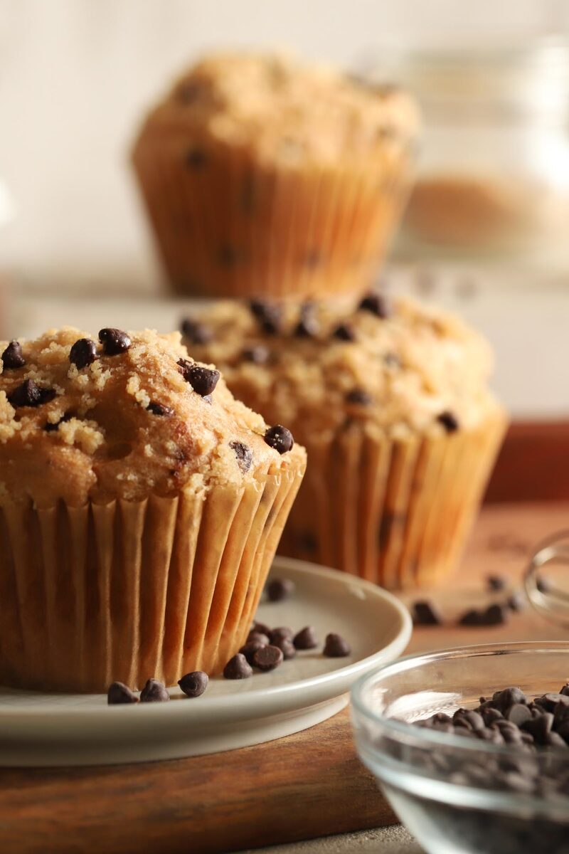 Chocolate chip muffins with streusel tops on a plate beside a bowl of chocolate chips