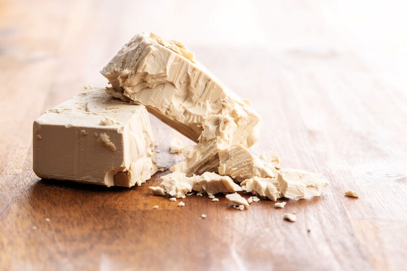 A broken block of fresh yeast on a wooden surface