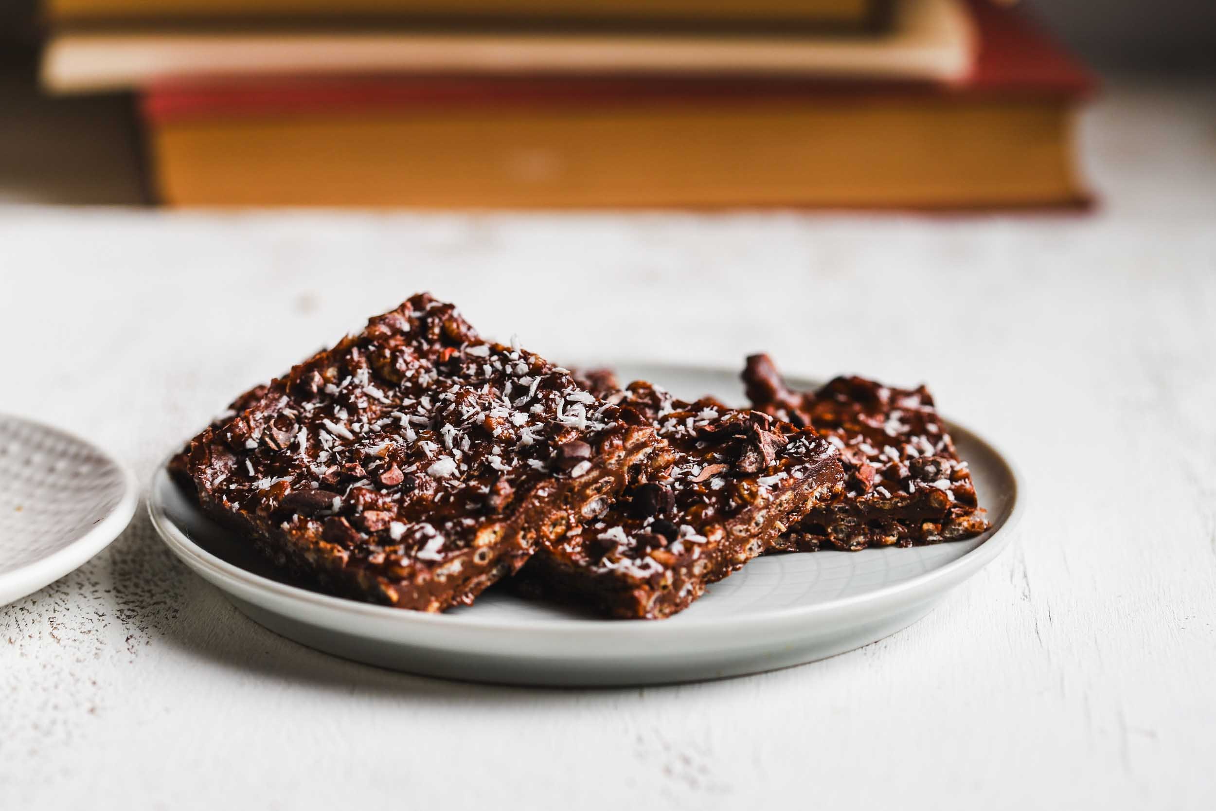 Frozen chocolate crunch bars stacked, topped with coconut and cacao nibs