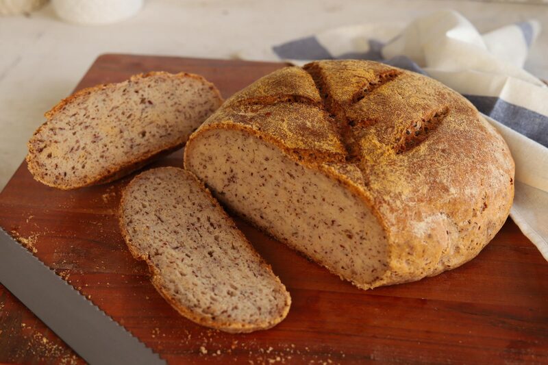A sliced gluten-free sourdough loaf on a wooden board, showing the soft interior crumb