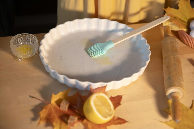Silicone pastry brush oiling a fluted white ceramic tart dish