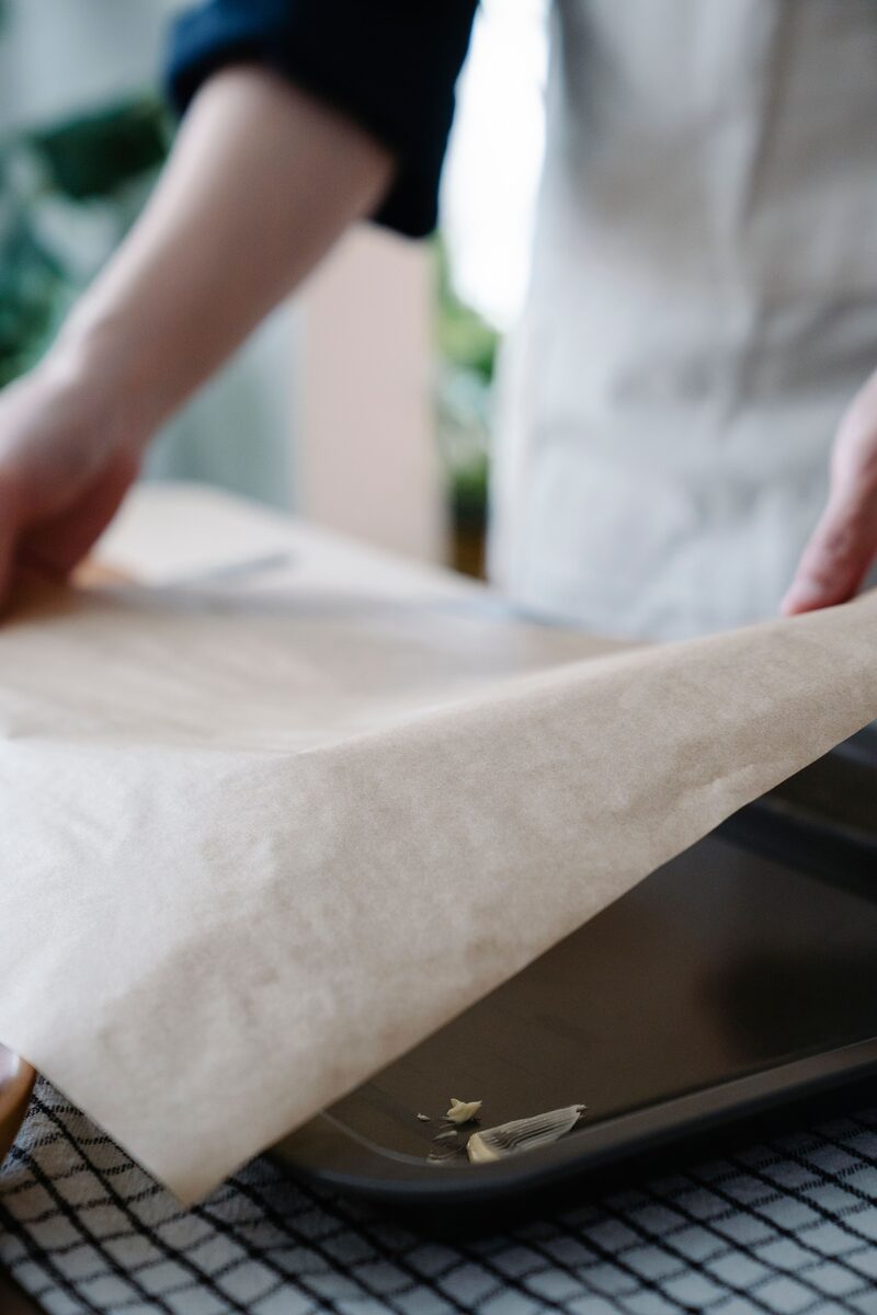 Baker lining a buttered metal baking pan with a sheet of parchment paper