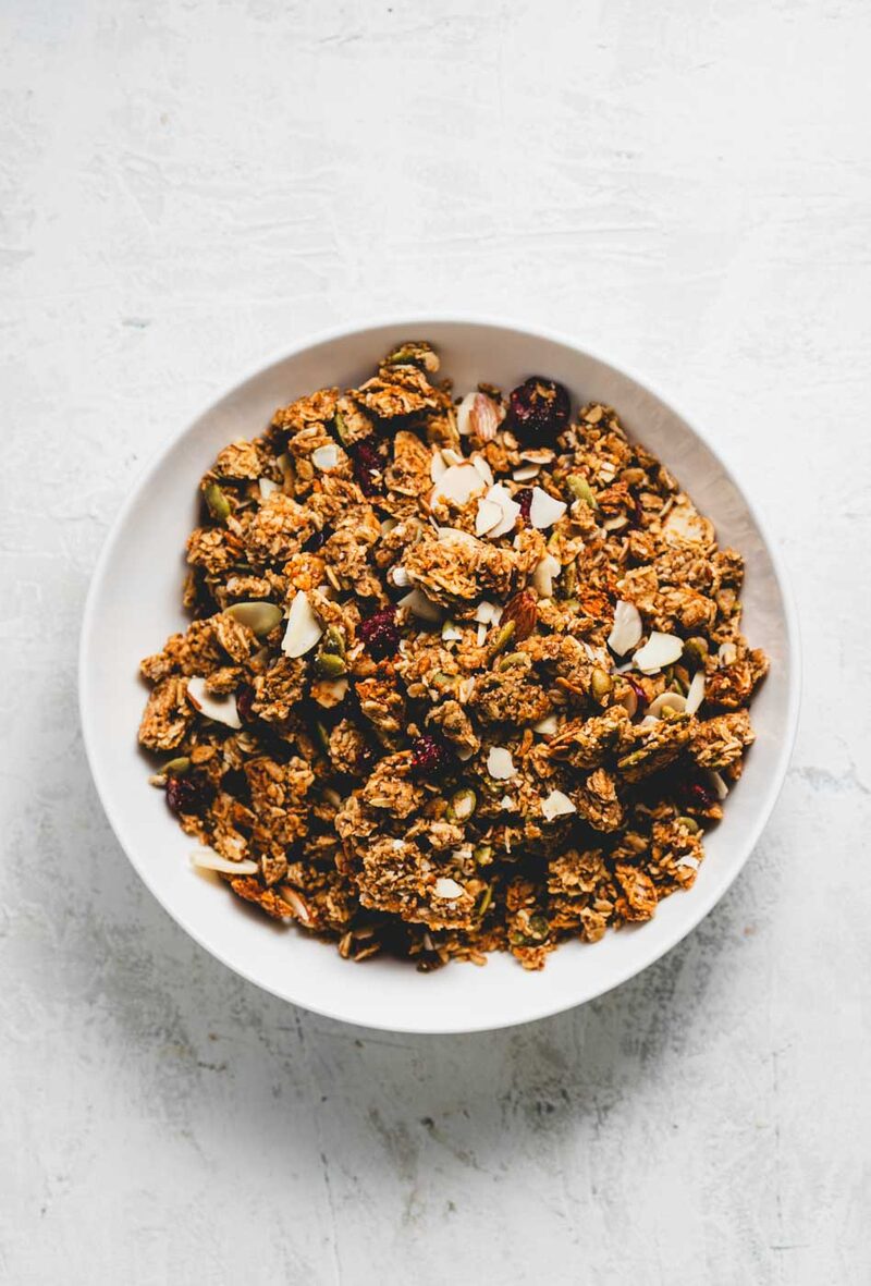 A white bowl of Sensible Bakery house granola with sliced almonds, pepitas, and cranberries