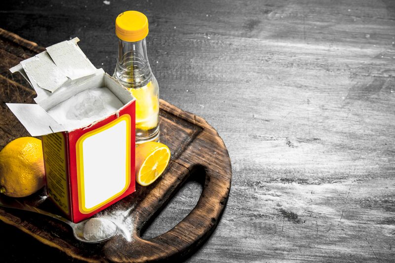 A box of baking soda on a wooden board with lemons and a bottle of vinegar