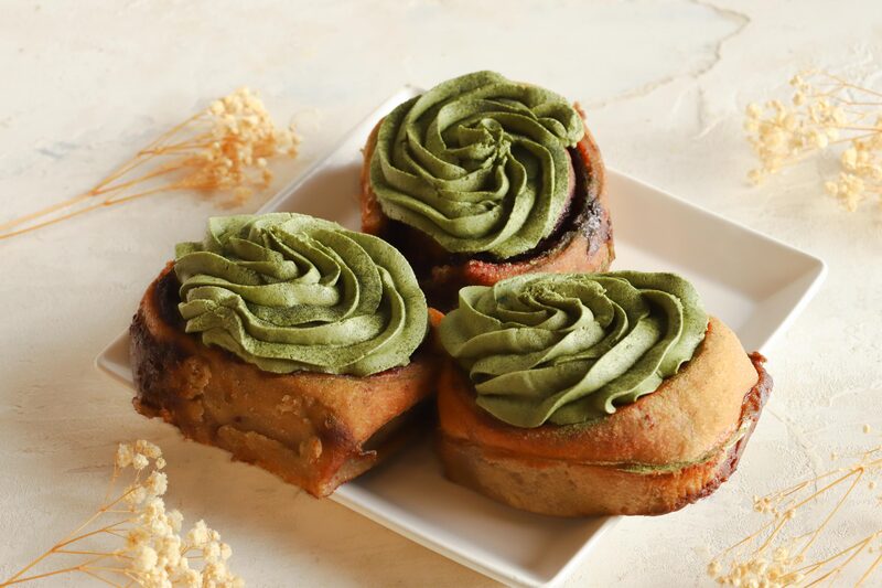 Three yeasted rolls topped with piped matcha frosting on a square white plate