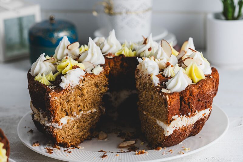 A tall layer cake cut open to show a light, evenly risen crumb, topped with piped frosting and sliced almonds