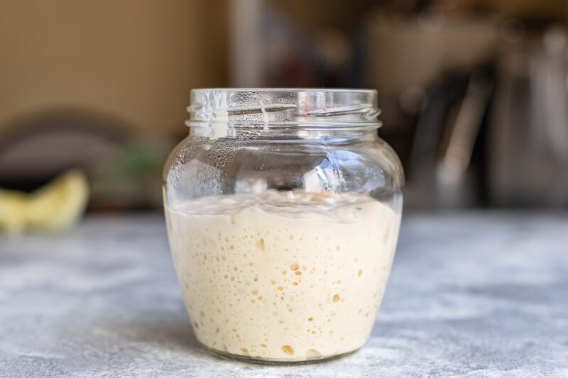 An active sourdough starter fermenting in a glass jar on a kitchen counter, full of bubbles