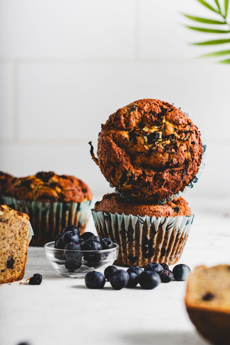 Two lemon zucchini protein muffins stacked, with blueberries scattered around