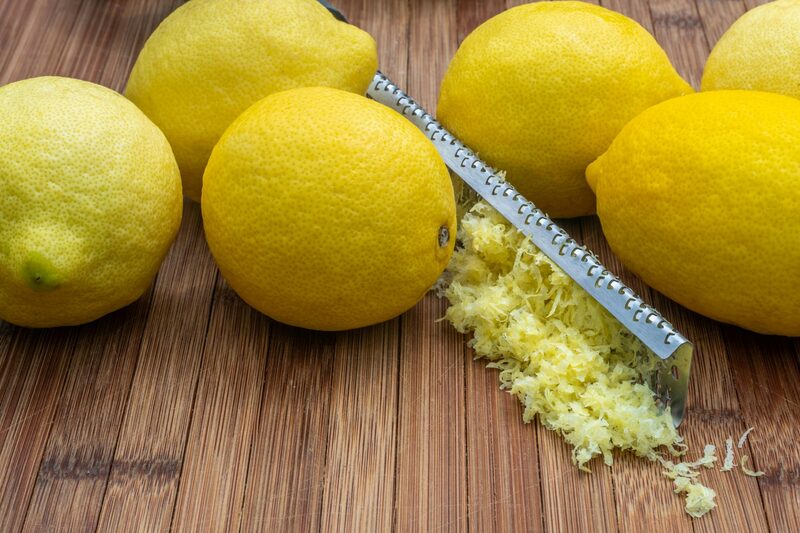 A grater full of lemon zest surrounded by fresh lemons