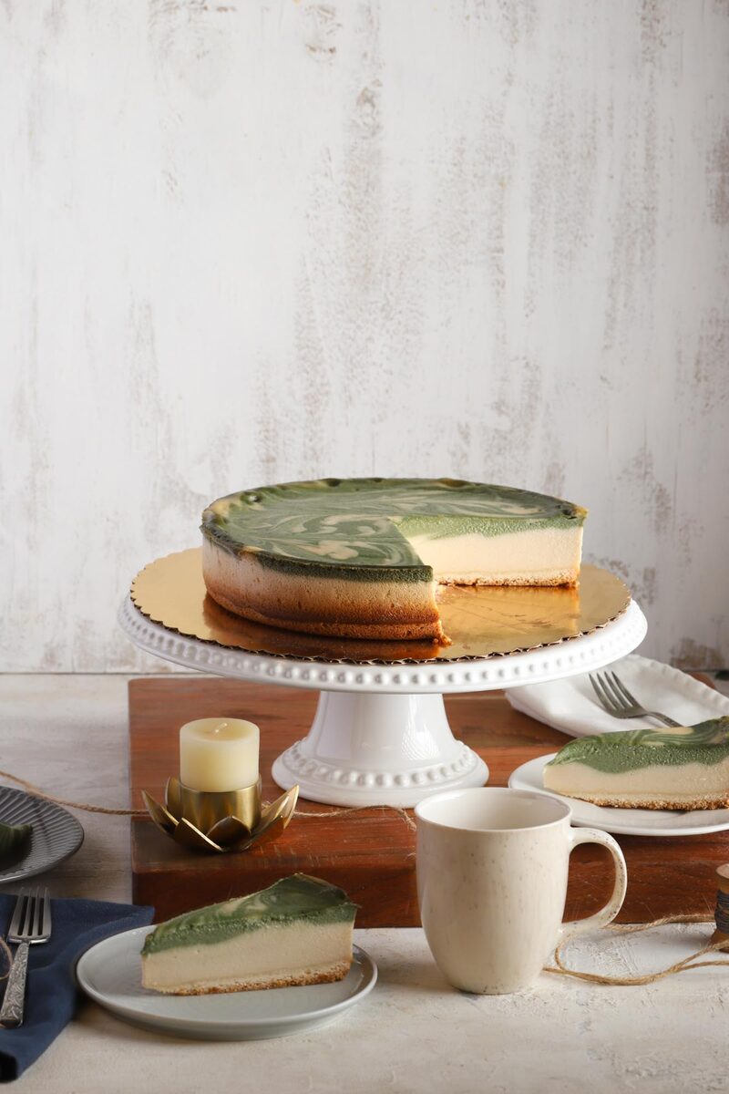 A matcha-swirled cheesecake on a cake stand with a slice cut and served