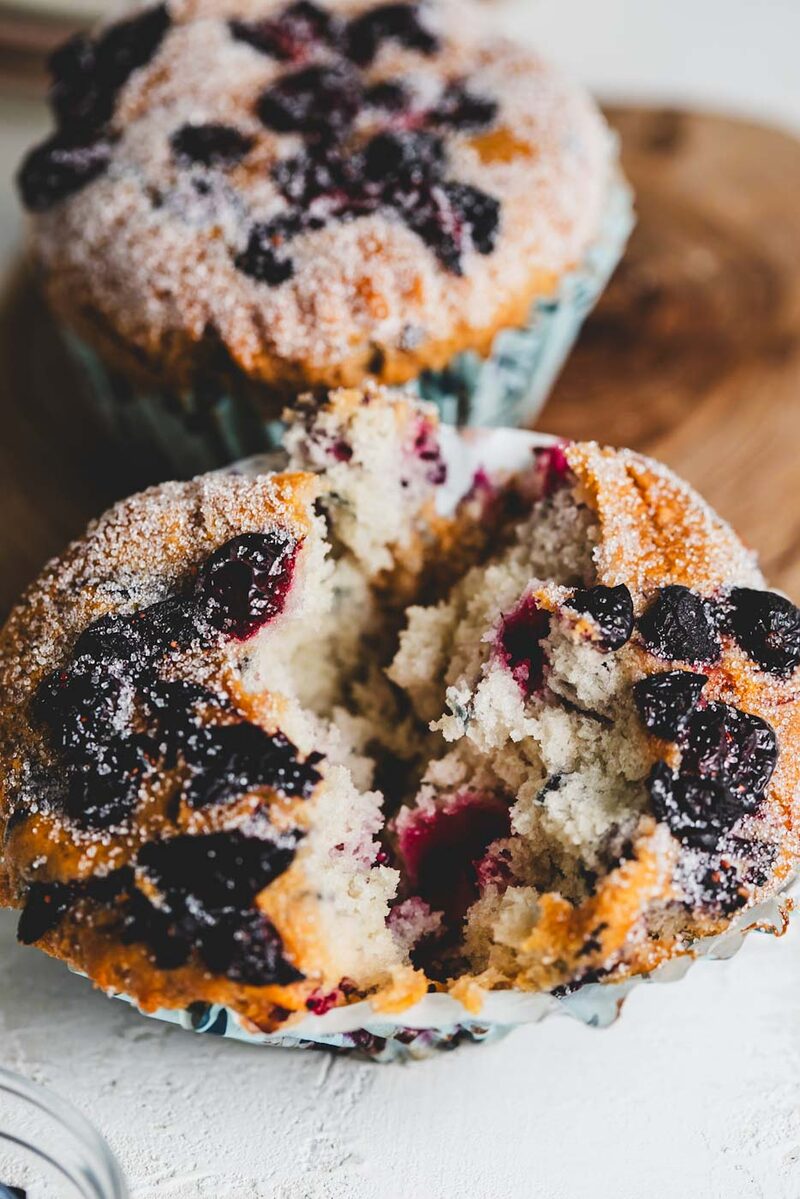 Blueberry muffins with one split open showing a soft, structured crumb