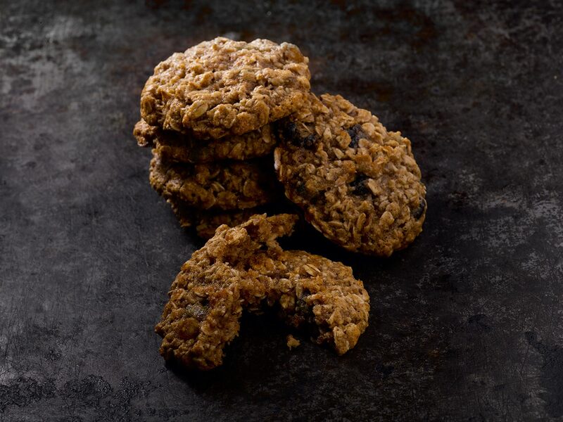 A stack of baked oatmeal raisin cookies with one broken in half on a dark baking sheet