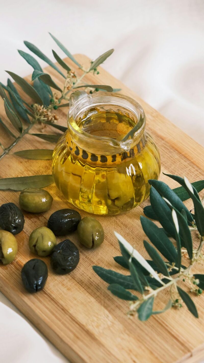 Jar of olive oil with green and black olives on a wood board