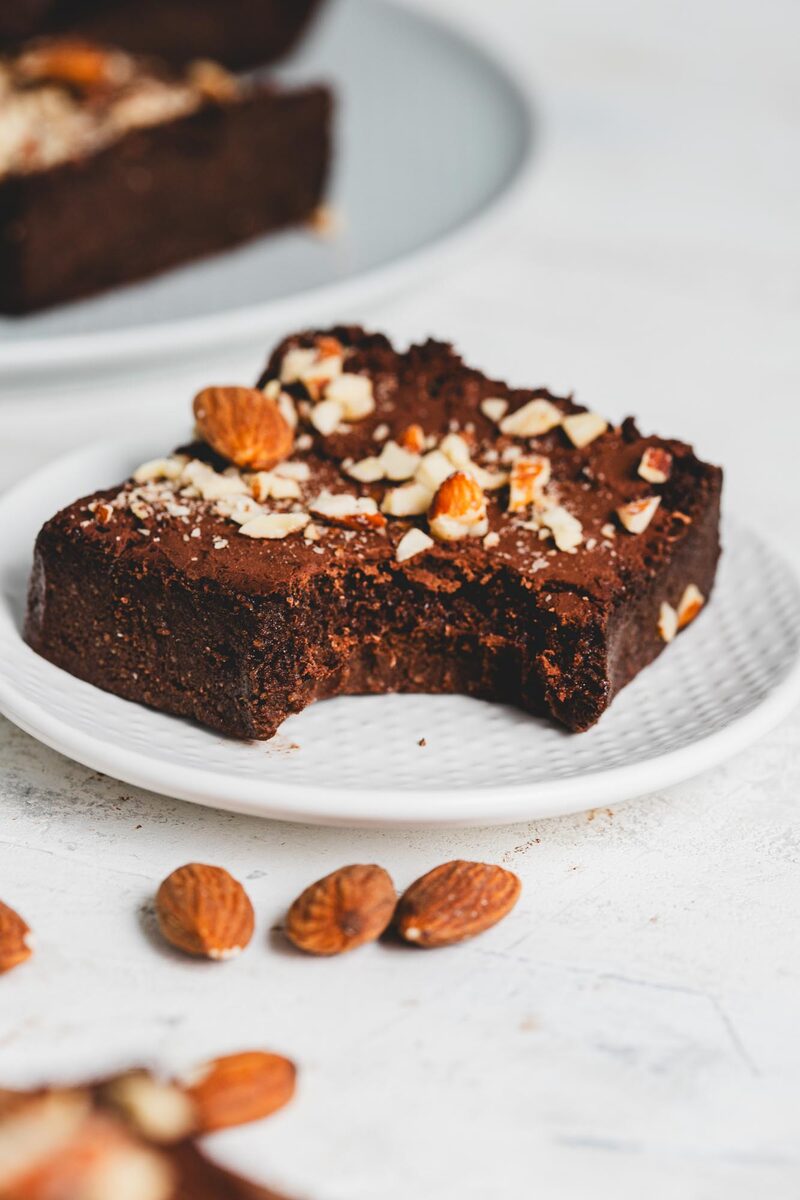 A protein brownie with a bite taken out, showing a fudgy interior, on a white plate
