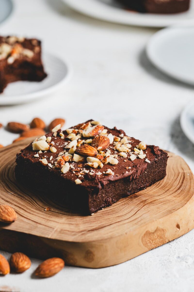 A fudgy sugar-free protein brownie topped with chopped almonds on a wooden board