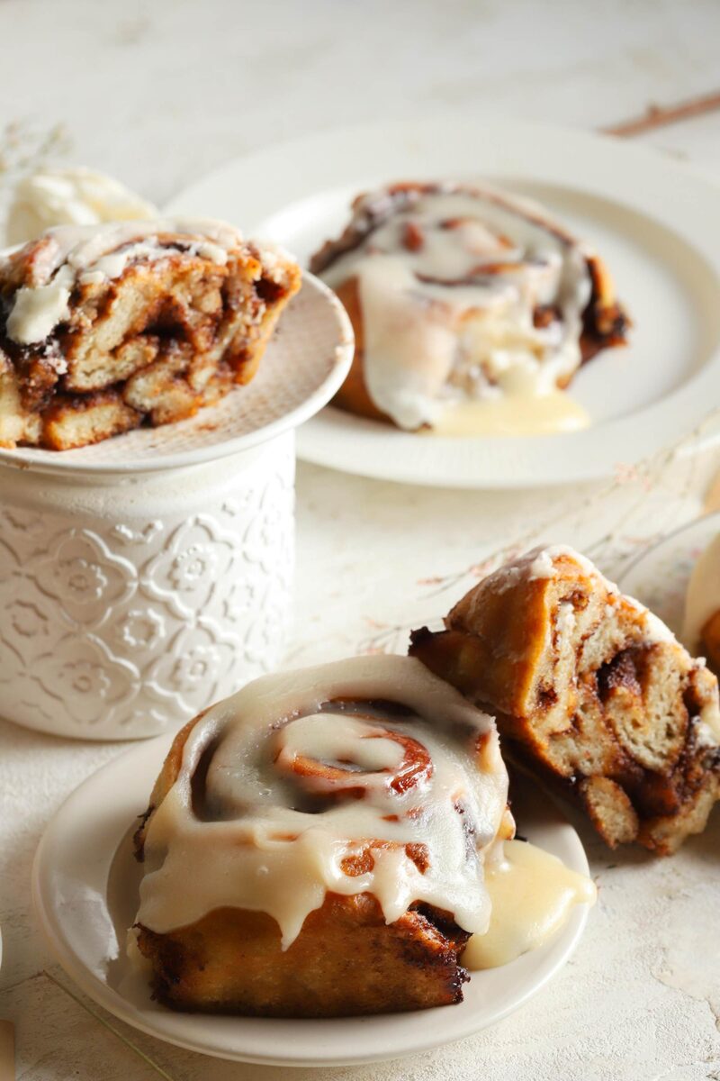 Cinnamon rolls glazed with icing, on plates and in a textured ceramic bowl