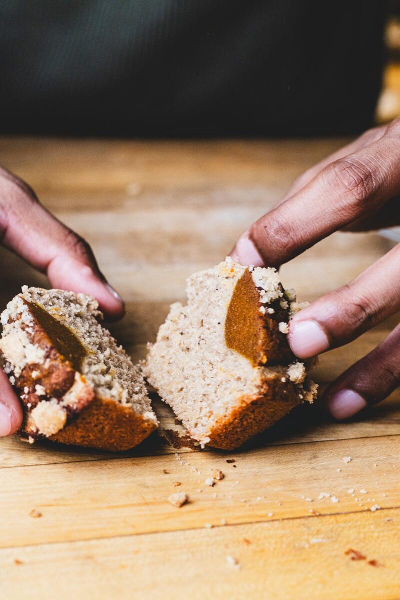 Hands breaking open a pumpkin pie muffin to reveal the pumpkin filling and crumb topping