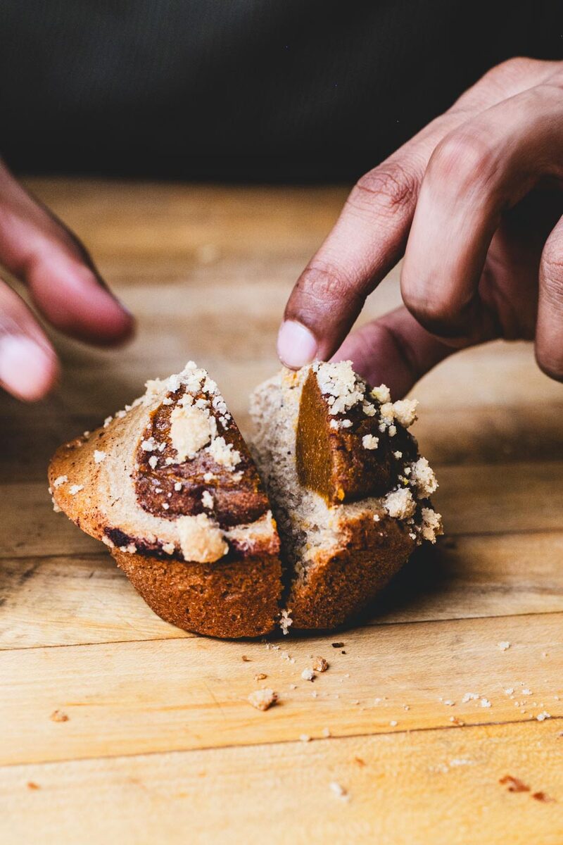 A single pumpkin pie muffin split open showing the pumpkin filling and crumb topping