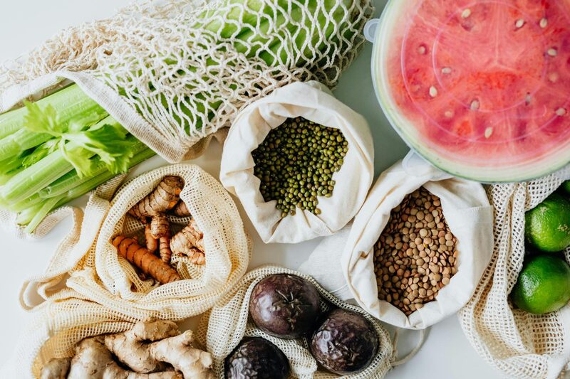 Reusable mesh produce bags filled with mung beans, lentils, ginger, and citrus next to celery and watermelon