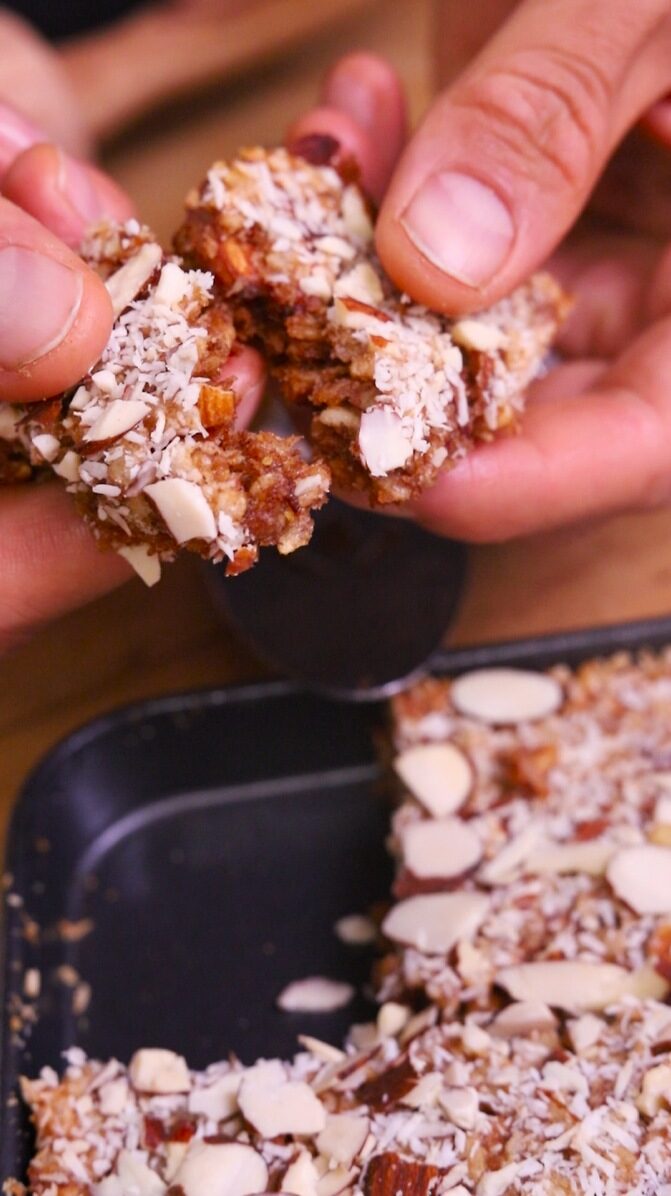 Hands breaking apart a rice krispie treat showing nuts and coconut