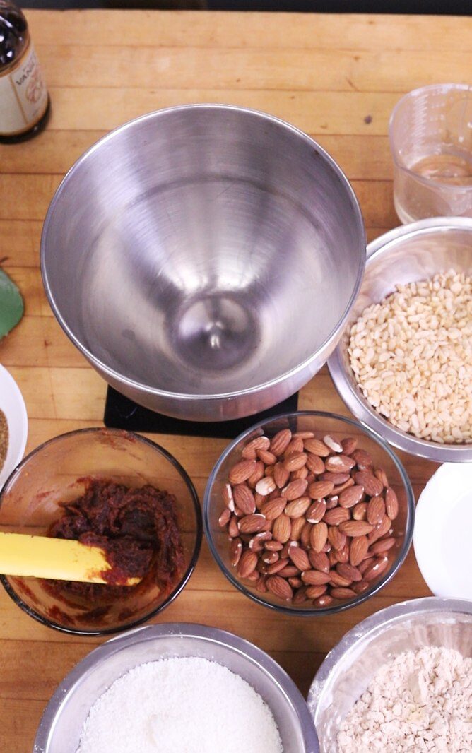 Bowls of dates, almonds, coconut, and rice cereal laid out on a wooden counter