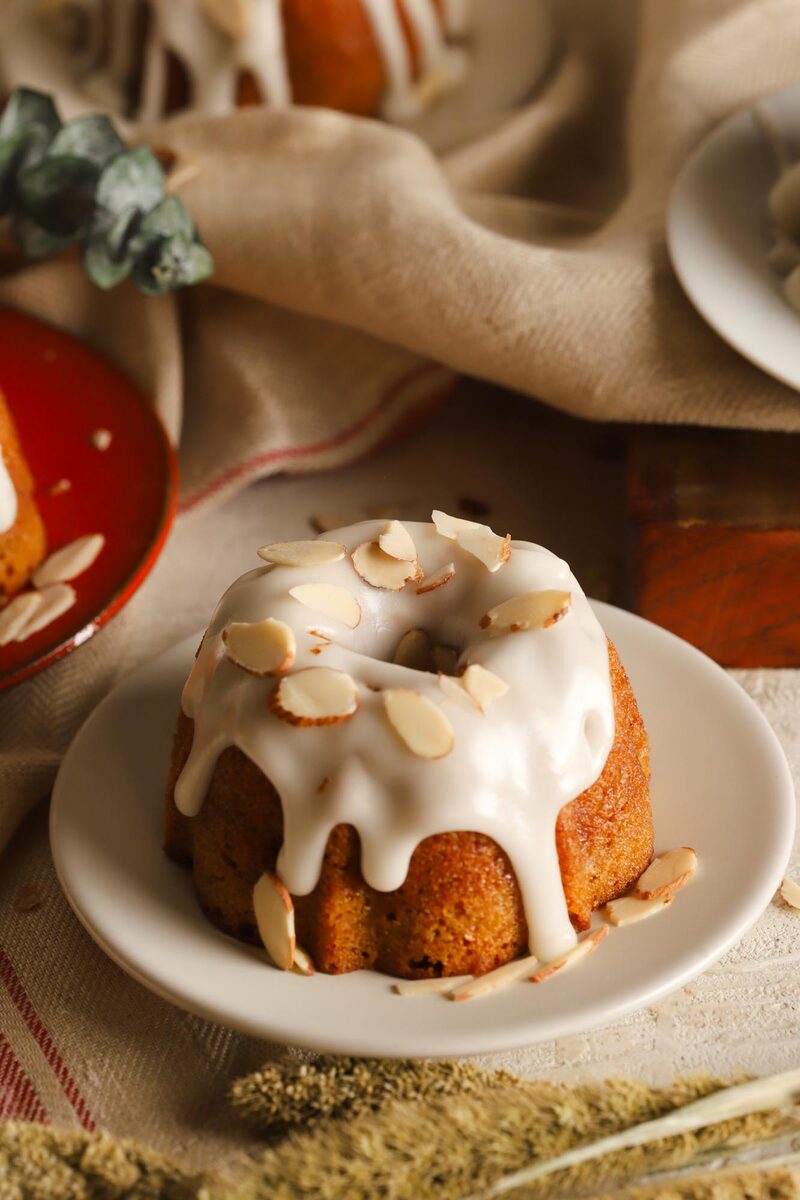 Mini almond bundt cake with white glaze and sliced almonds on a plate