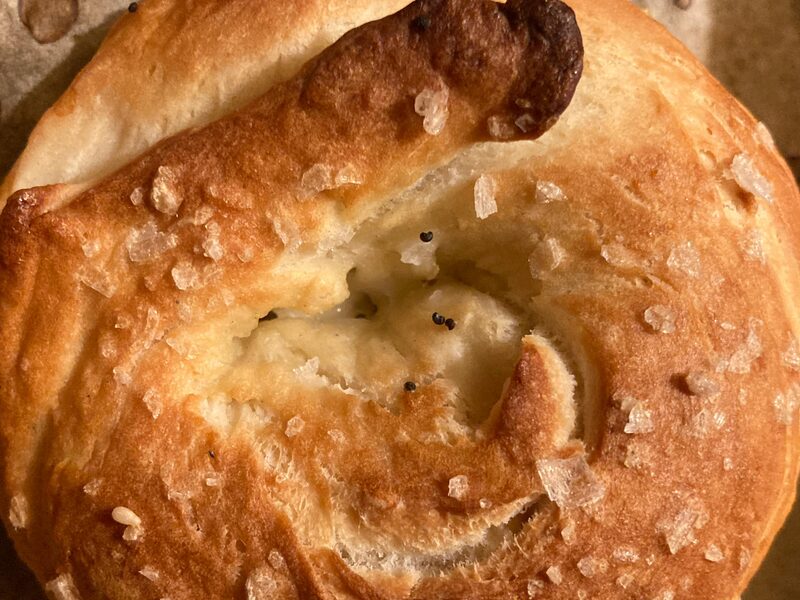 Golden-brown bread roll topped with coarse salt crystals and nigella seeds