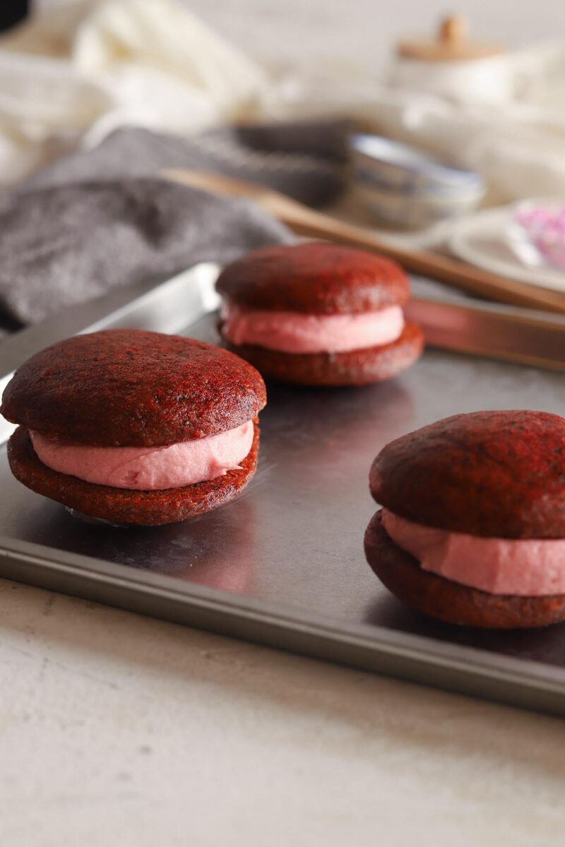 Red velvet whoopie pies with pink cream filling on a baking sheet